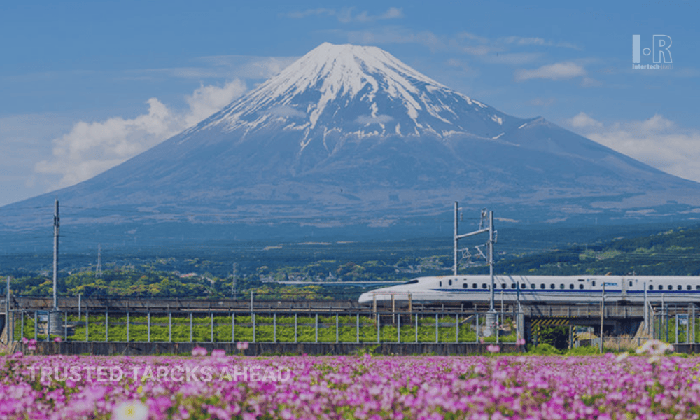 A bullet train speeding past pink flowers with Mt. Fuji in the background.