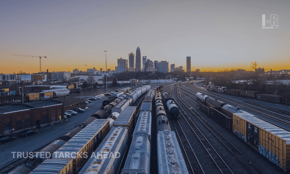 Trains in a railyard with a city skyline at sunset.