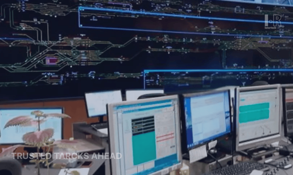 Control room with multiple computer screens displaying data, a large screen showing network diagrams, and the text