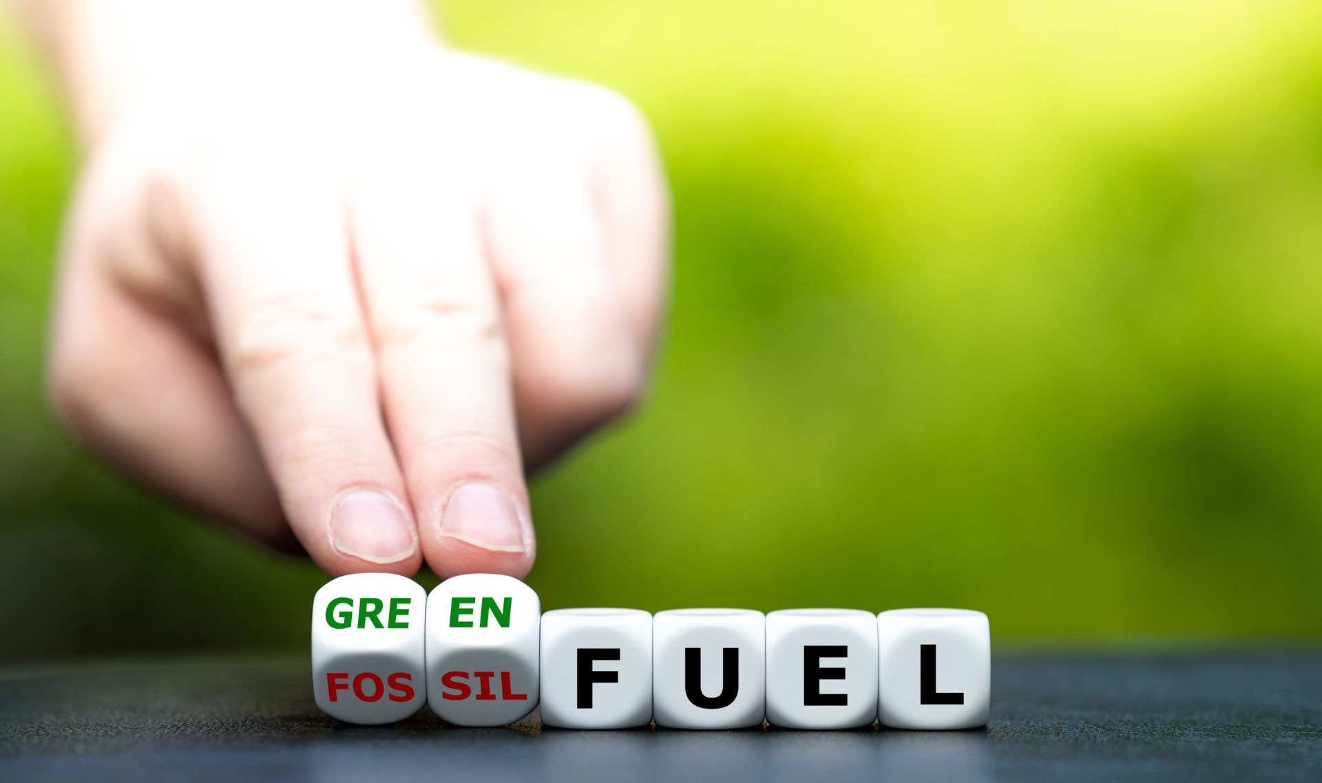 hand touching dices with the word green and the word fossil next to dices forming the word fuel.
