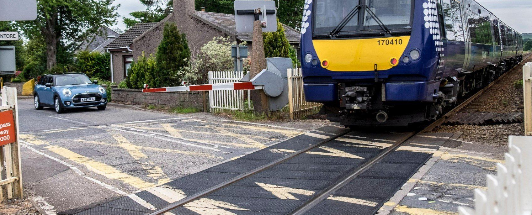 Photograph of train under tracks while a car waits for the level crossing gate to open