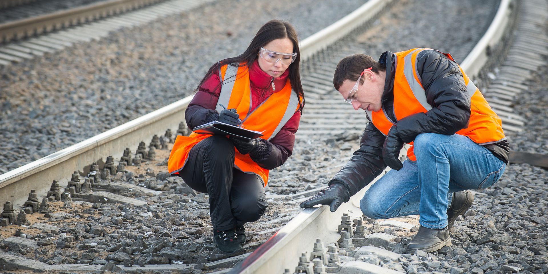 two people with orange coats checking the safety of the train tracks