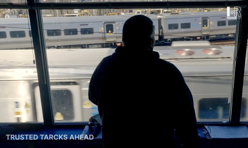 Silhouetted person looking out a window at a passing train, with a “Trusted tacks ahead” sign in the corner