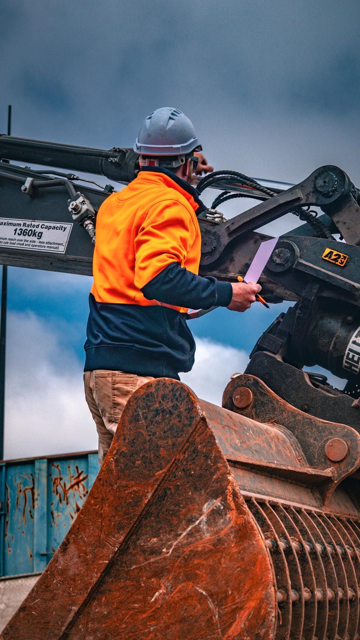 Construction worker in orange safety vest and hard hat examines a purple document next to excavator — Murphy's Salvage & Demolition in Baranduda, VIC