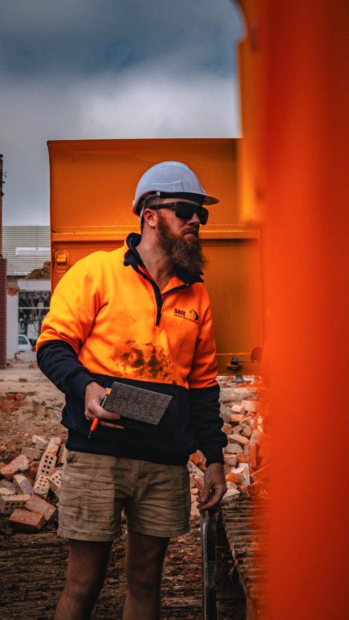 Construction worker in safety vest and hard hat holding a tool, standing near orange construction equipment — Murphy's Salvage & Demolition in Baranduda, VIC