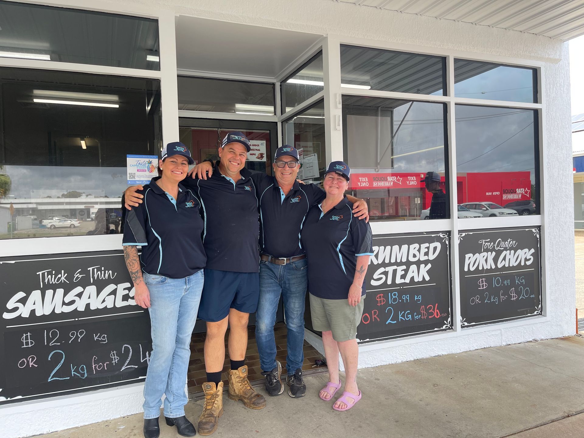 Four People in Matching Blue Shirts and Hats Stand Outside a Butcher Shop — Coastal Meats in Yeppoon, QLD