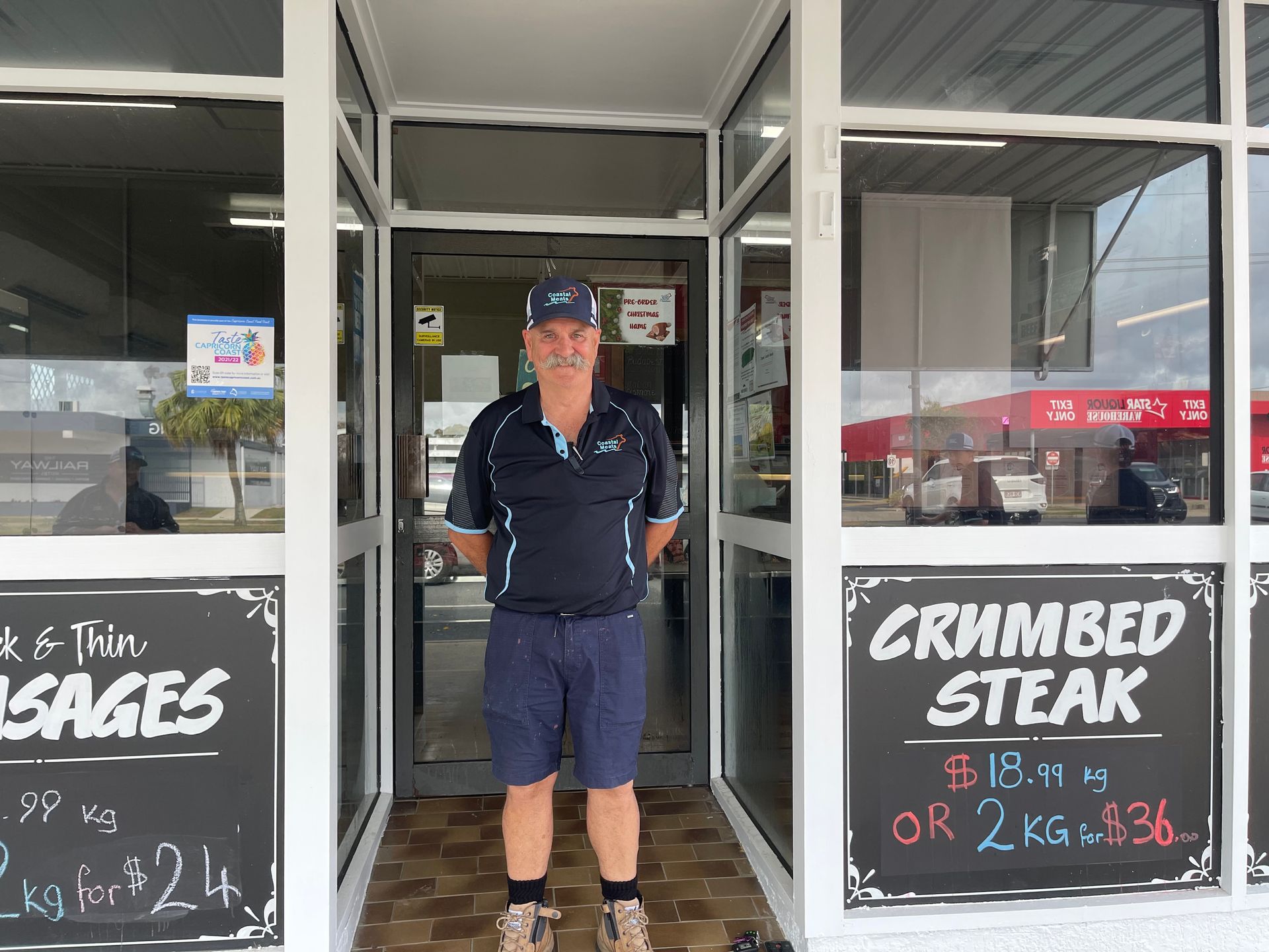 Man Stands in the Doorway of a Butcher Shop, Wearing a Cap and Shorts — Coastal Meats in Yeppoon, QLD