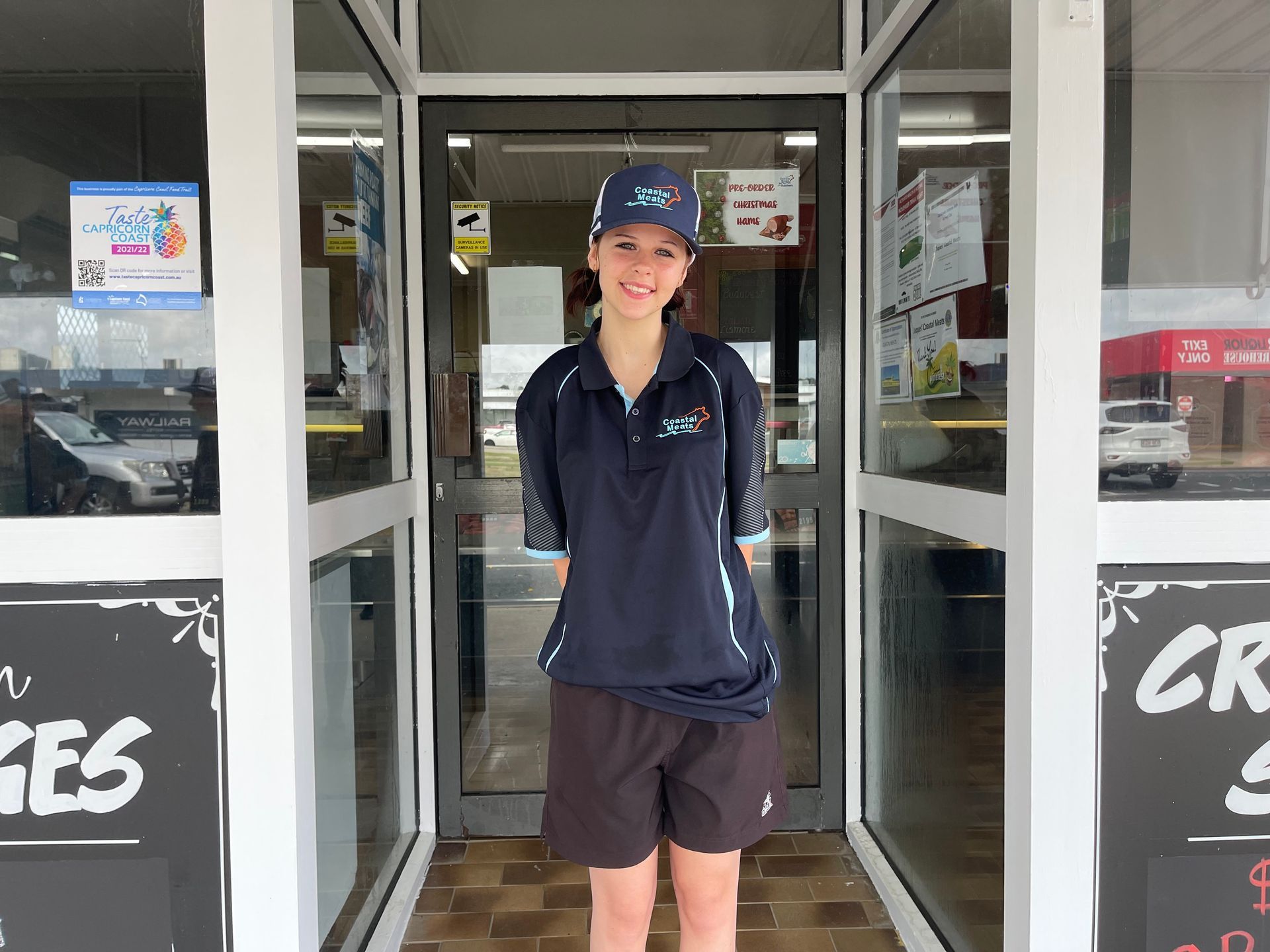 A Young Woman in a Uniform Stands in a Butcher Shop Doorway — Coastal Meats in Yeppoon, QLD