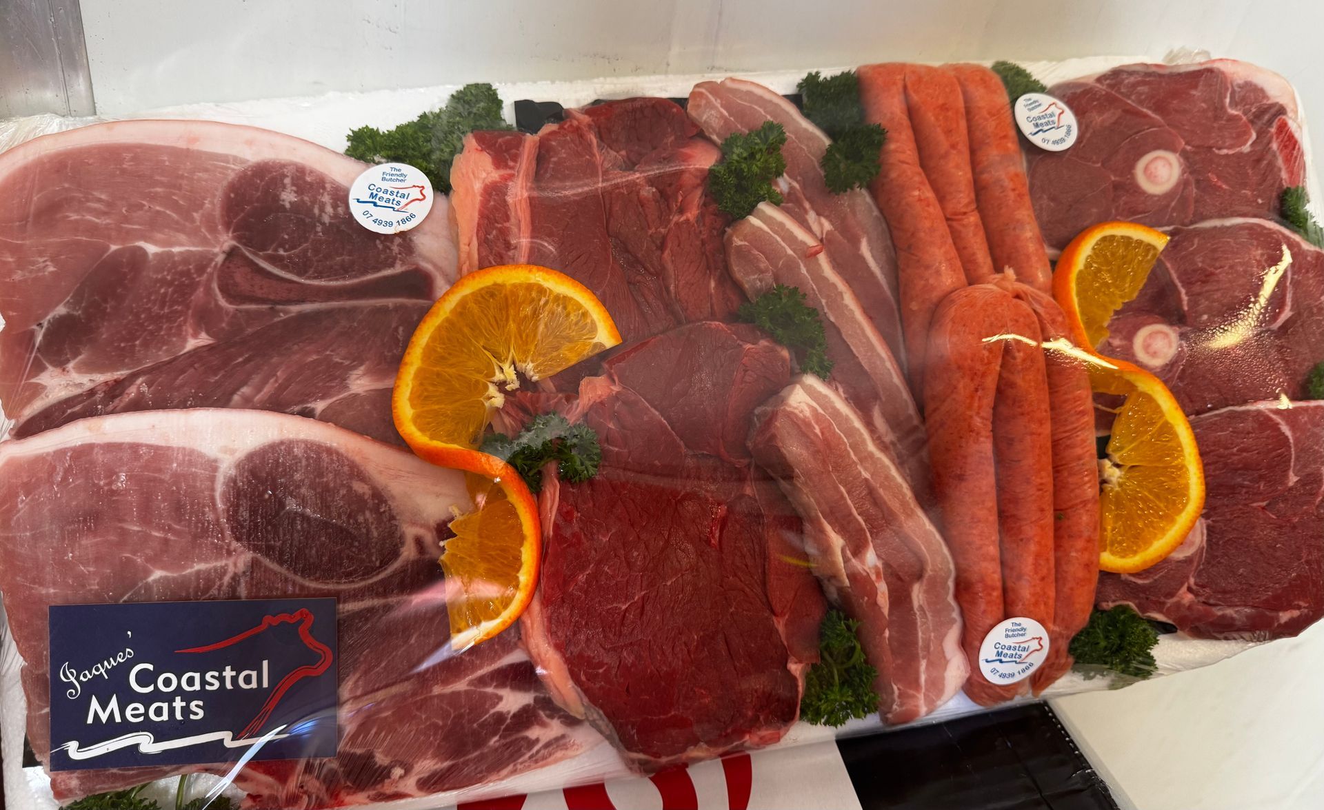 Butcher in a Black Shirt and Apron Smiles, Holding a Packed Meat Platter in a Butcher Shop — Coastal Meats in Yeppoon, QLD