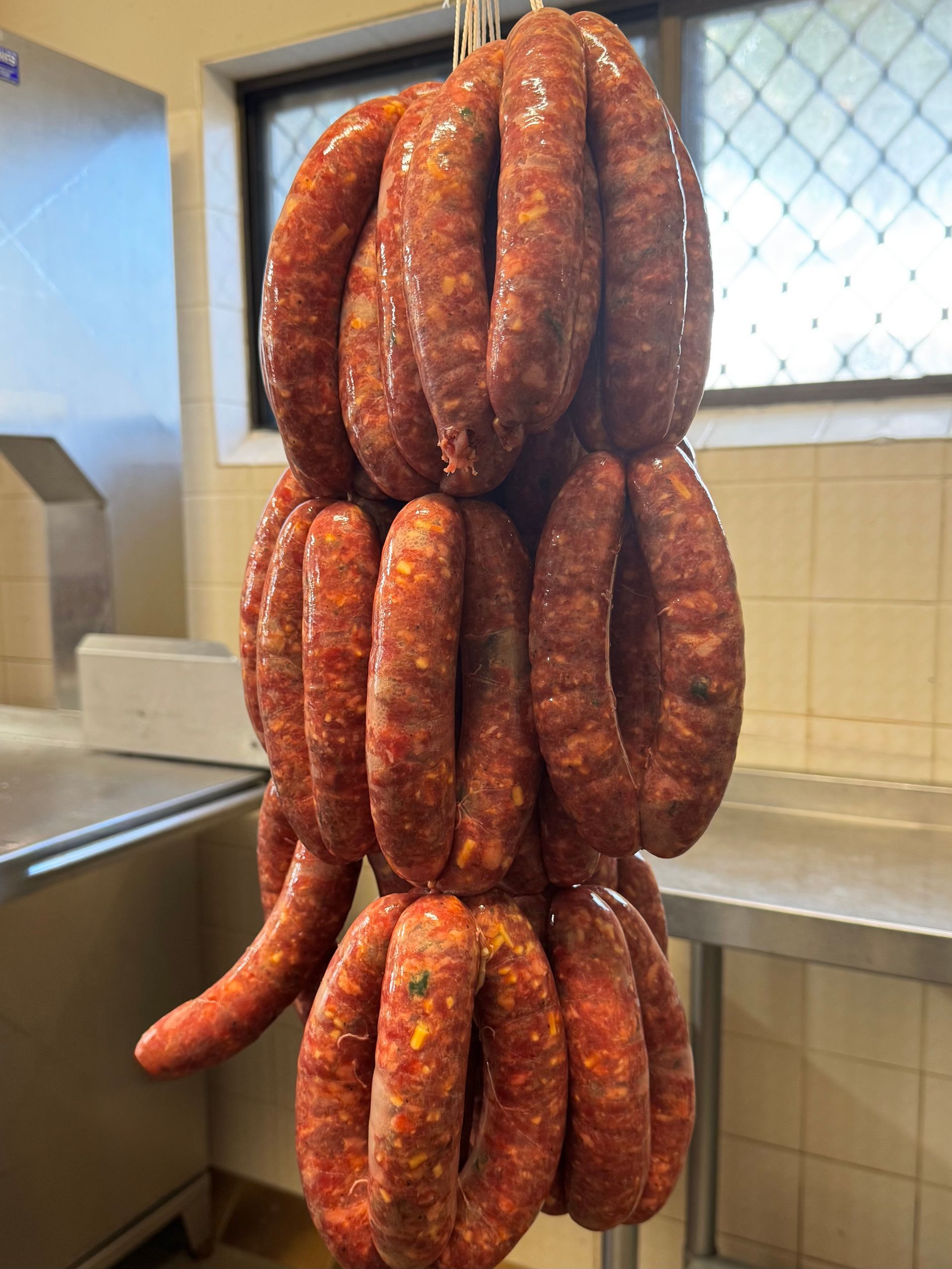 Sausages hanging in a butcher shop, red and orange colours, rings of sausage linked together — Coastal Meats in Yeppoon, QLD