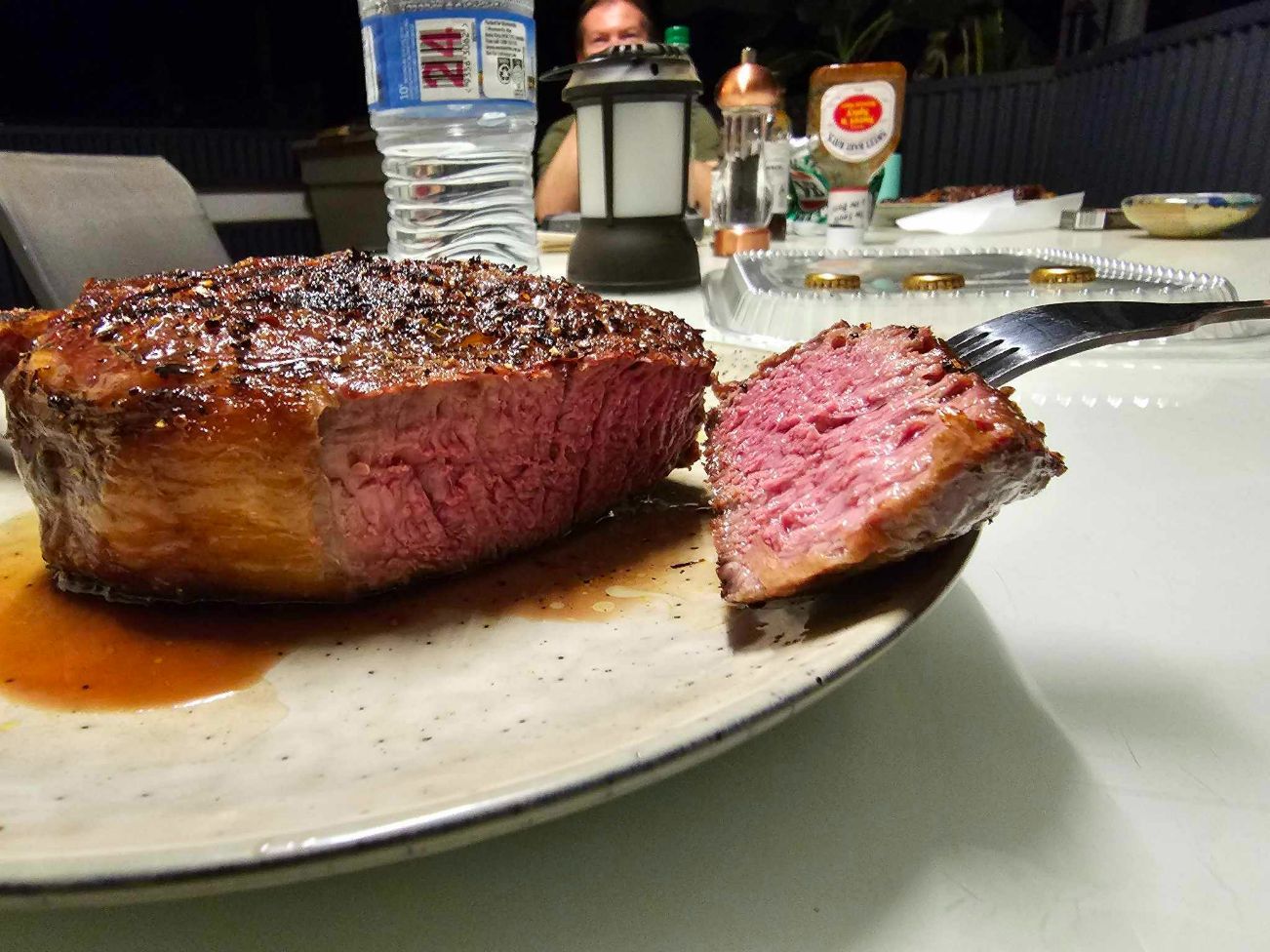 A Medium-rare Steak On A Plate, Being Cut With A Fork, With A Person And Outdoor Setting — Coastal Meats in Yeppoon, QLD