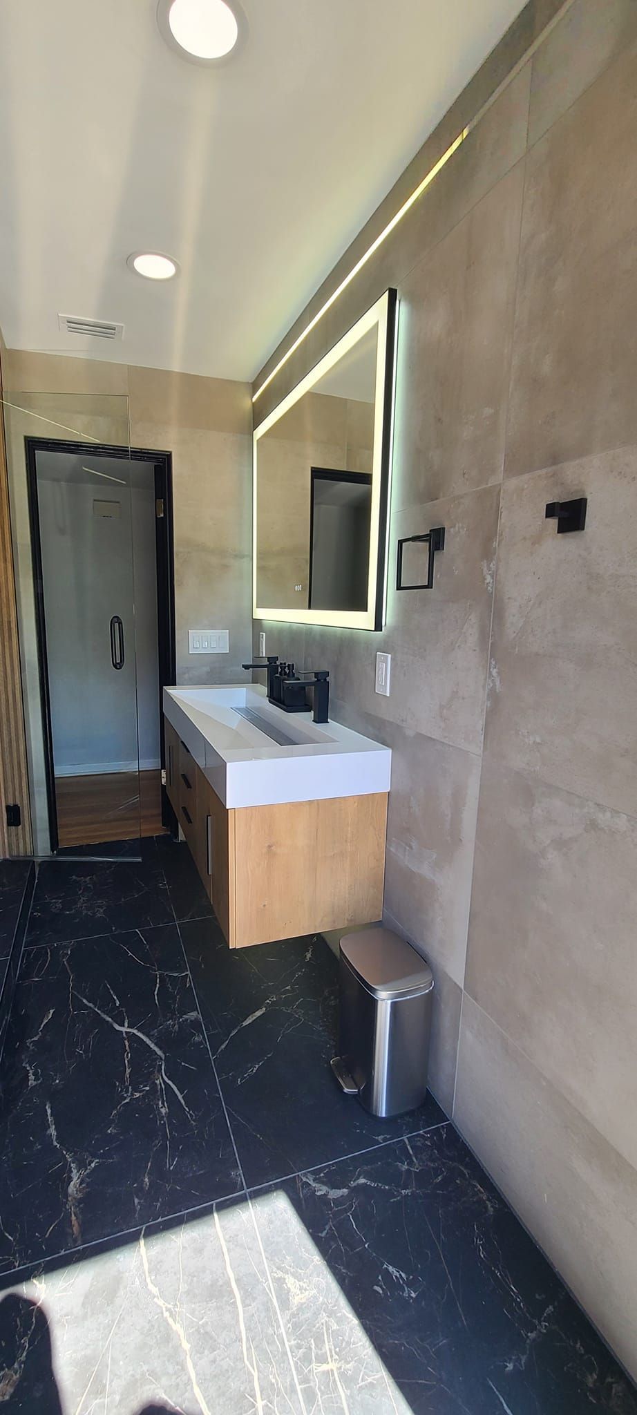 A bathroom with a sink , mirror and trash can.