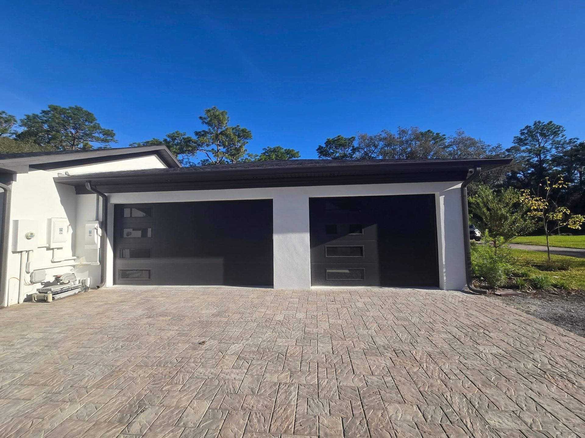 A white house with two black garage doors and a brick driveway.