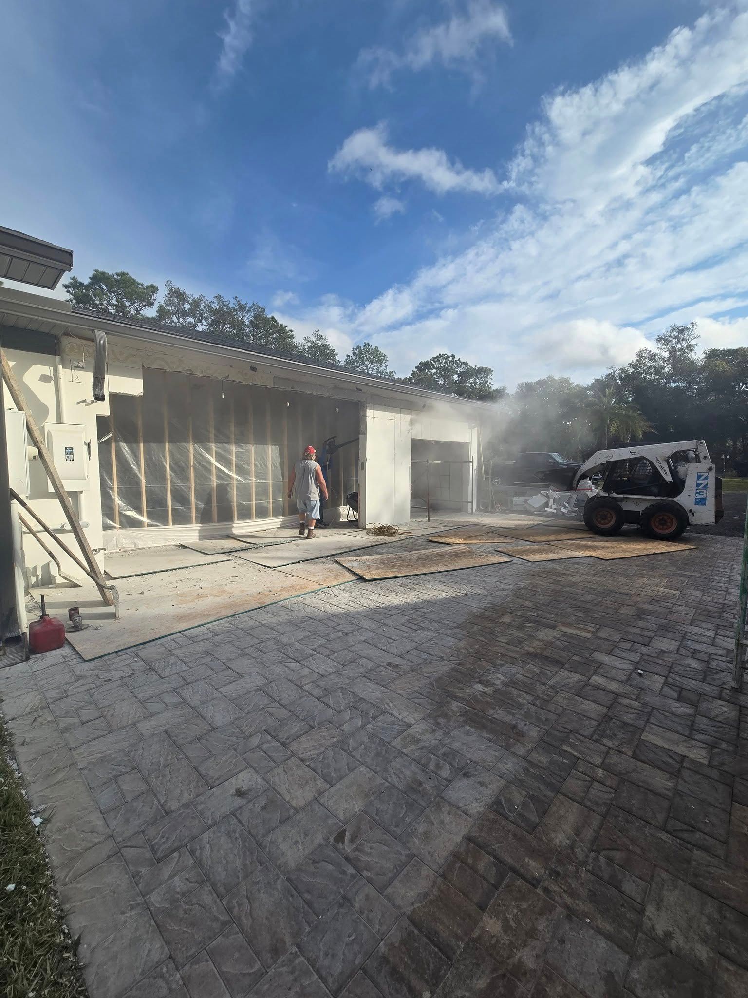 A bobcat is cleaning the sidewalk in front of a house.