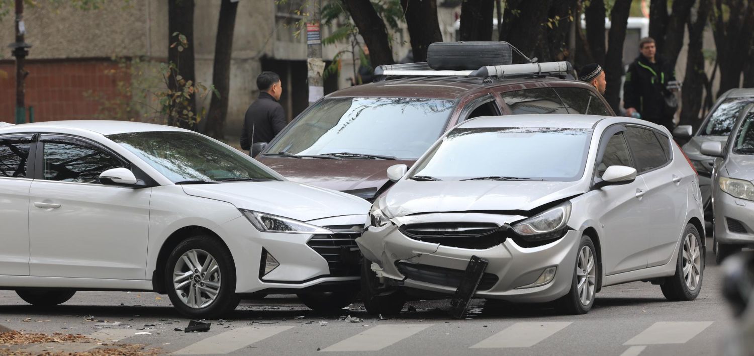Cars involved in a collision on a crosswalk; damaged white and silver cars, a brown SUV, and people nearby.