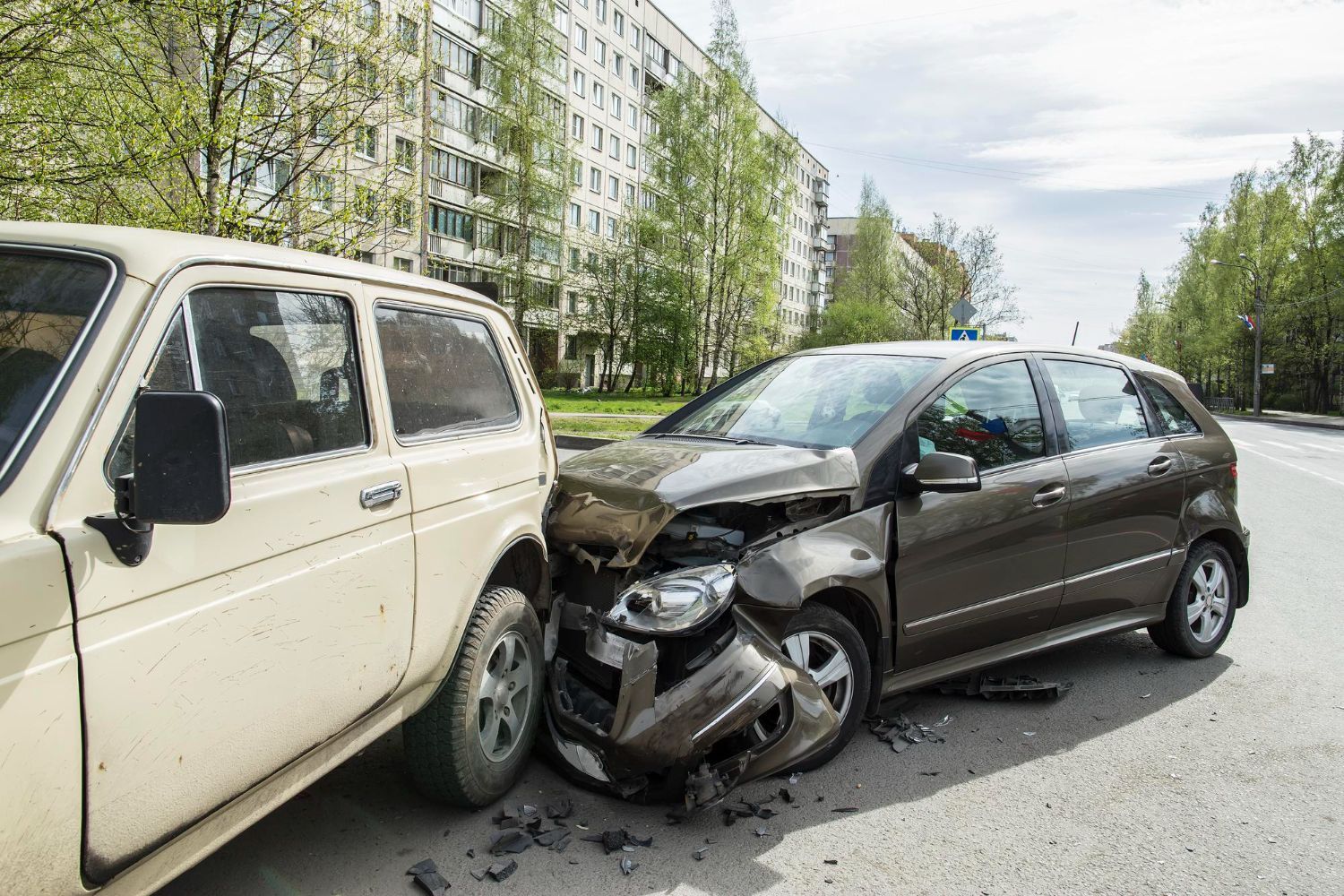 Two cars damaged in a collision on a city street; a tan SUV and a brown hatchback.