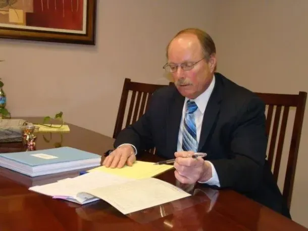 Man in suit, sitting at desk, reviewing papers, with pen in hand.