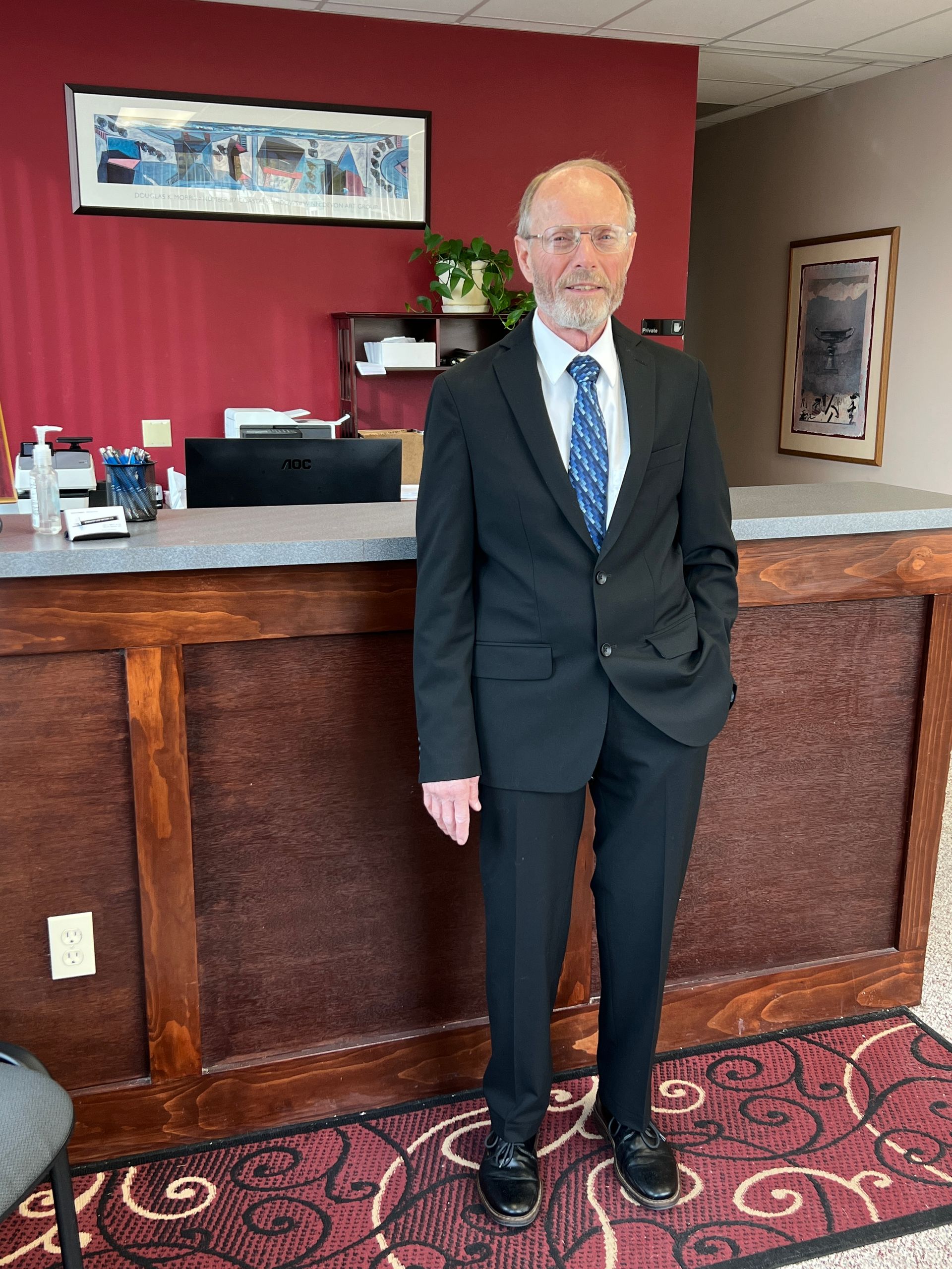 Man in suit, sitting at desk, reviewing papers, with pen in hand.