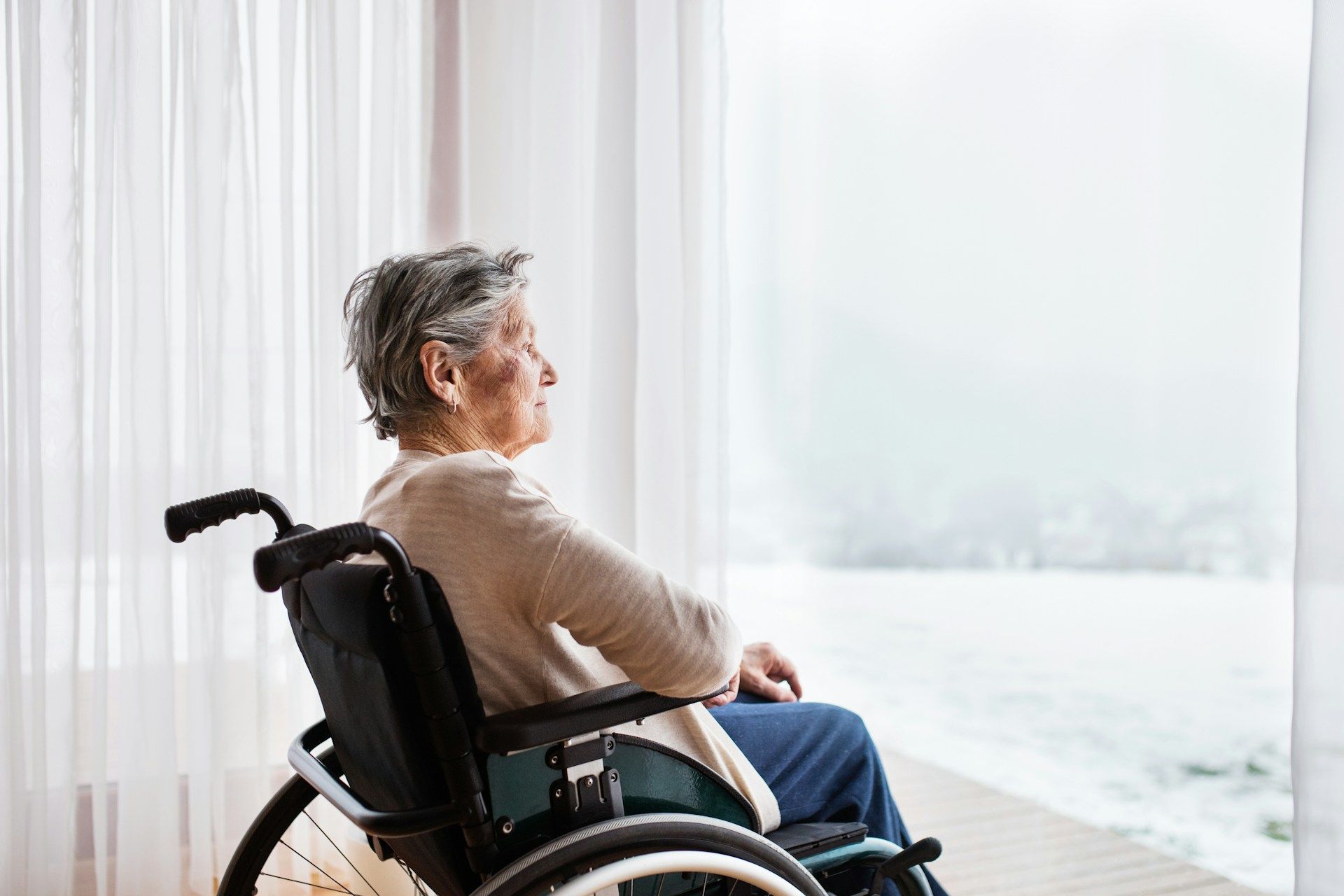 Woman in wheelchair looking out window at a misty view.