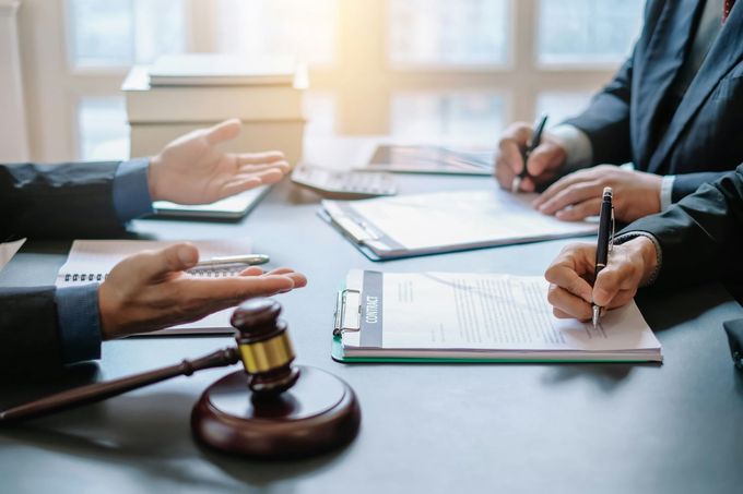 Legal professionals in suits at a table with documents, a gavel, and calculators; discussing.