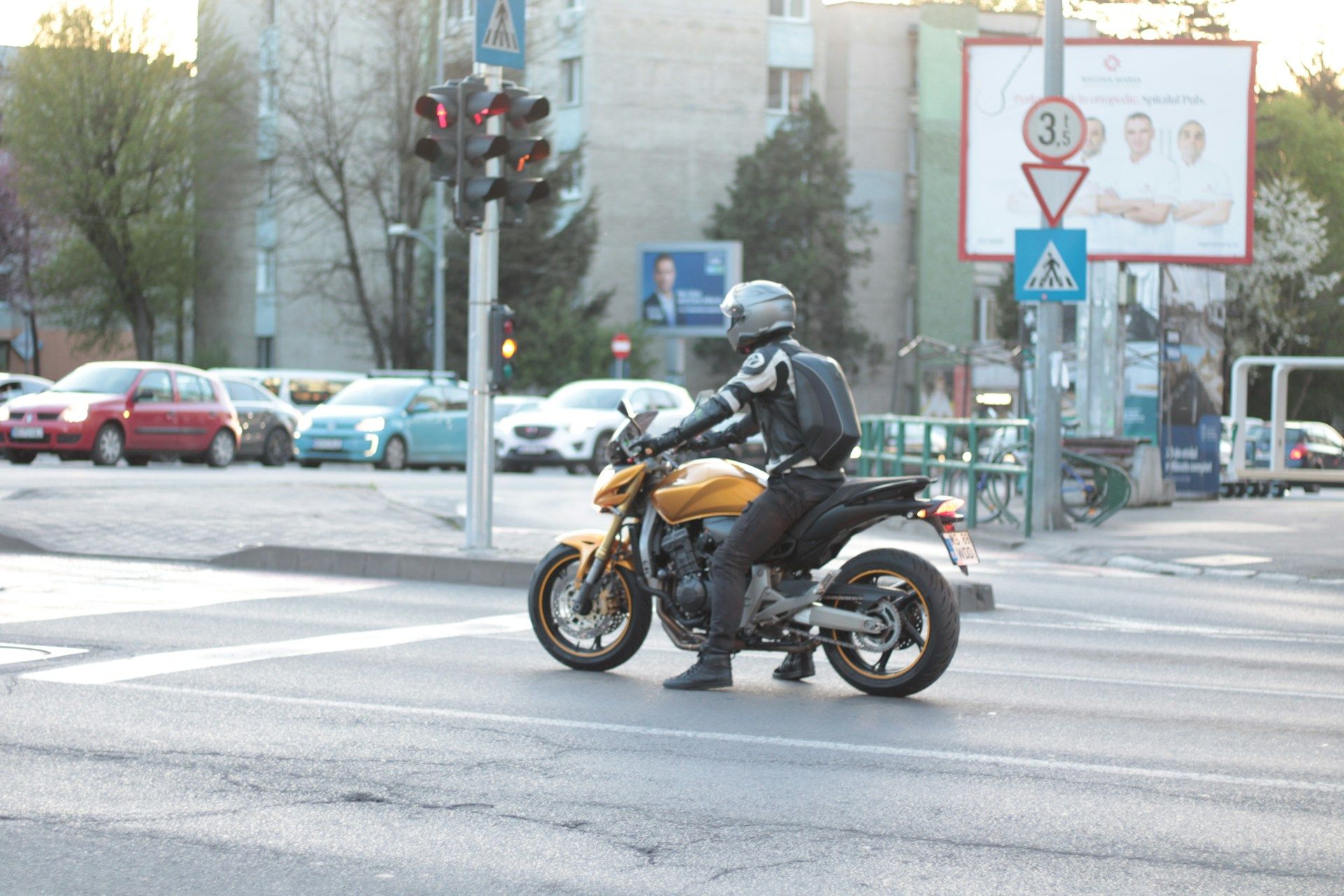 Motorcyclist on a yellow motorcycle waiting at a red traffic light on a city street.
