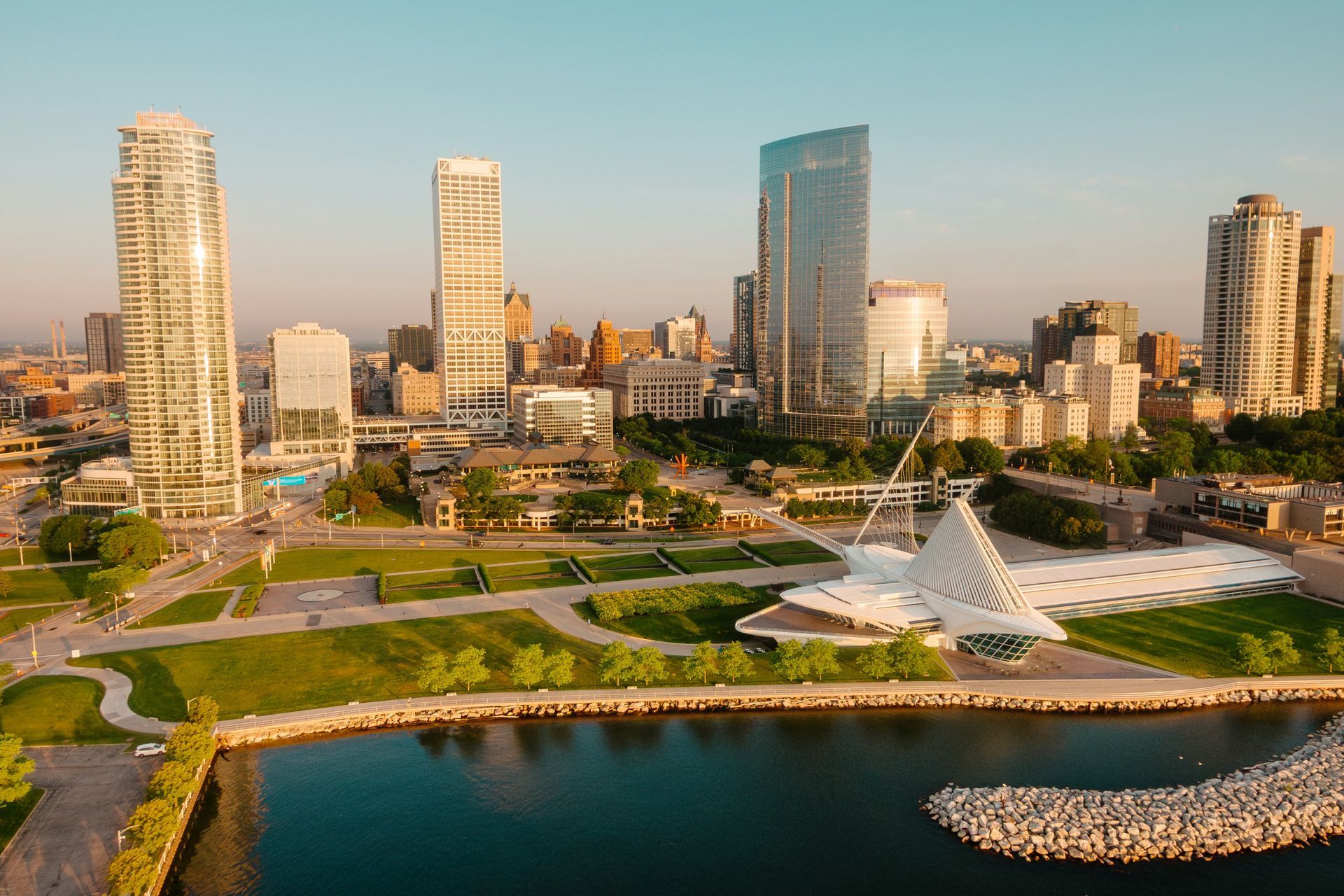 Milwaukee skyline with skyscrapers, lake, and white art museum under blue sky.