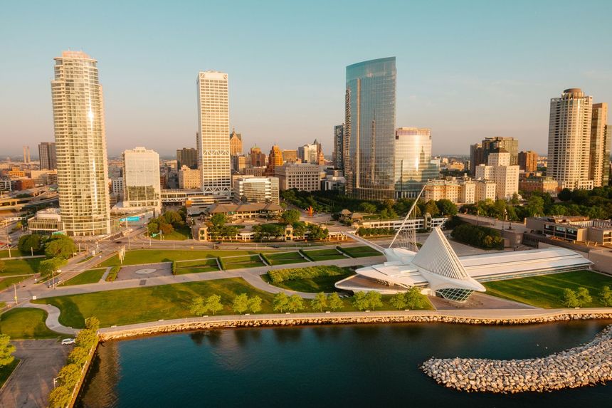 Milwaukee skyline with skyscrapers, lake, and white art museum under blue sky.