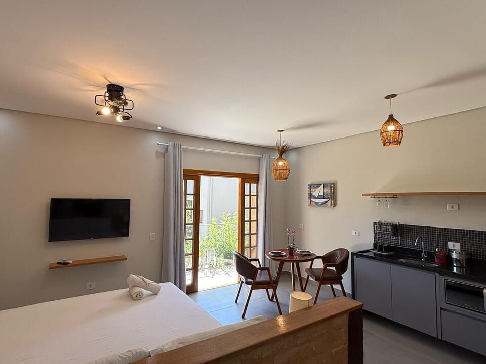 Um estúdio moderno com uma cama, uma mesa de jantar para duas pessoas e uma kitchenette compacta em tons de cinza escuro.