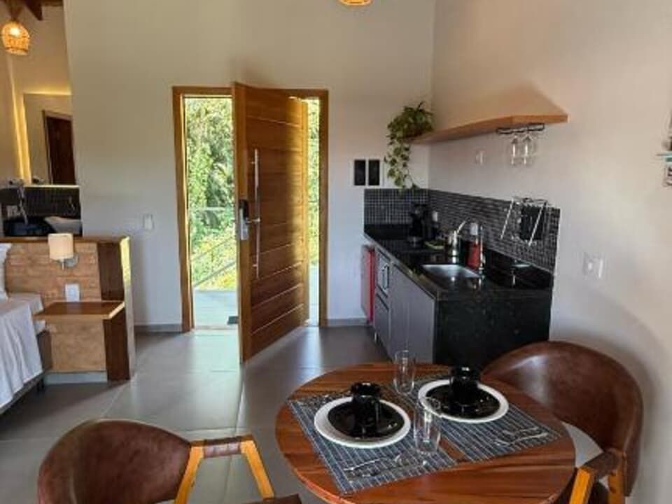 Interior de um moderno apartamento estúdio com cozinha compacta, mesa de jantar para duas pessoas e porta com vista para o exterior.