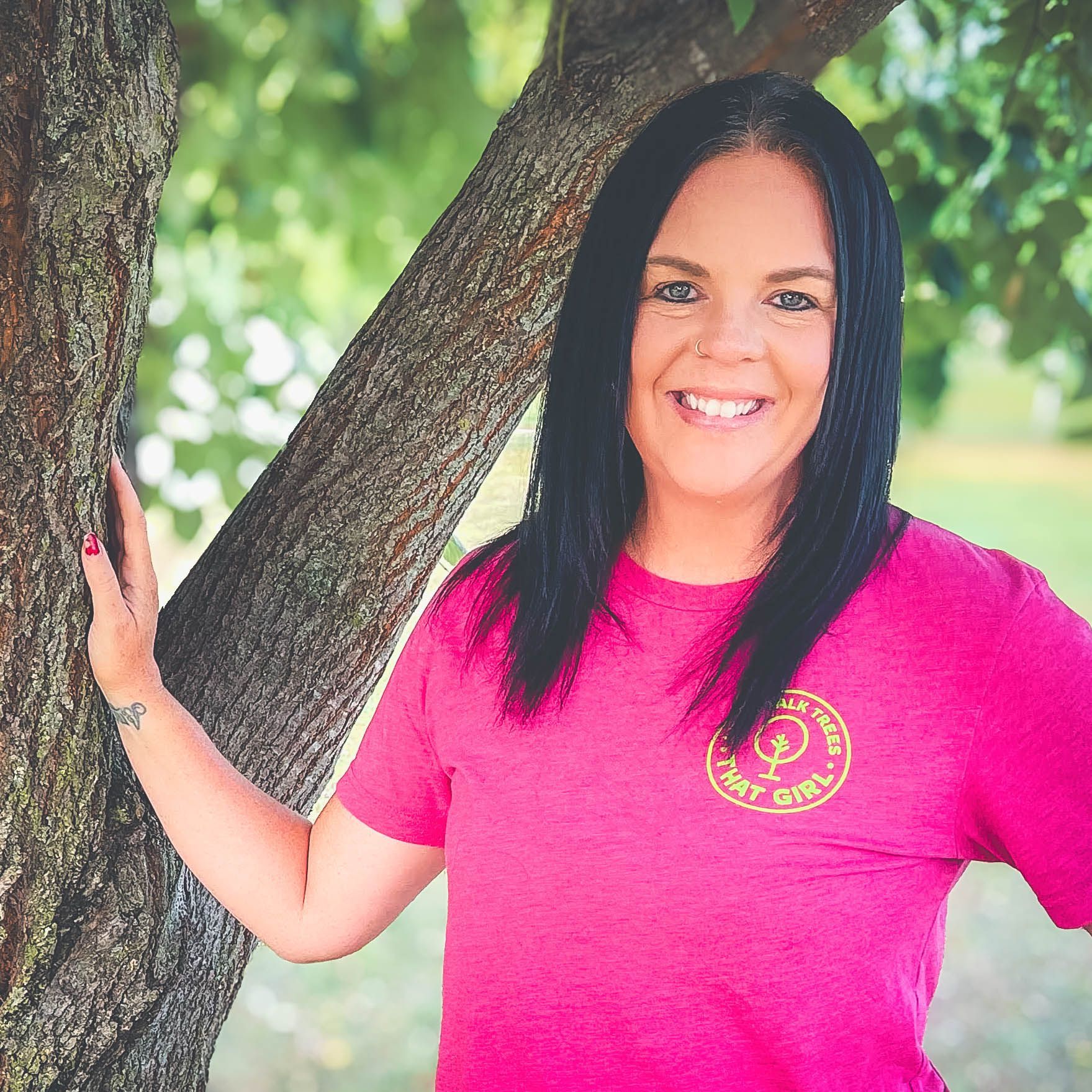 A woman in a pink shirt is smiling while talking on a phone.