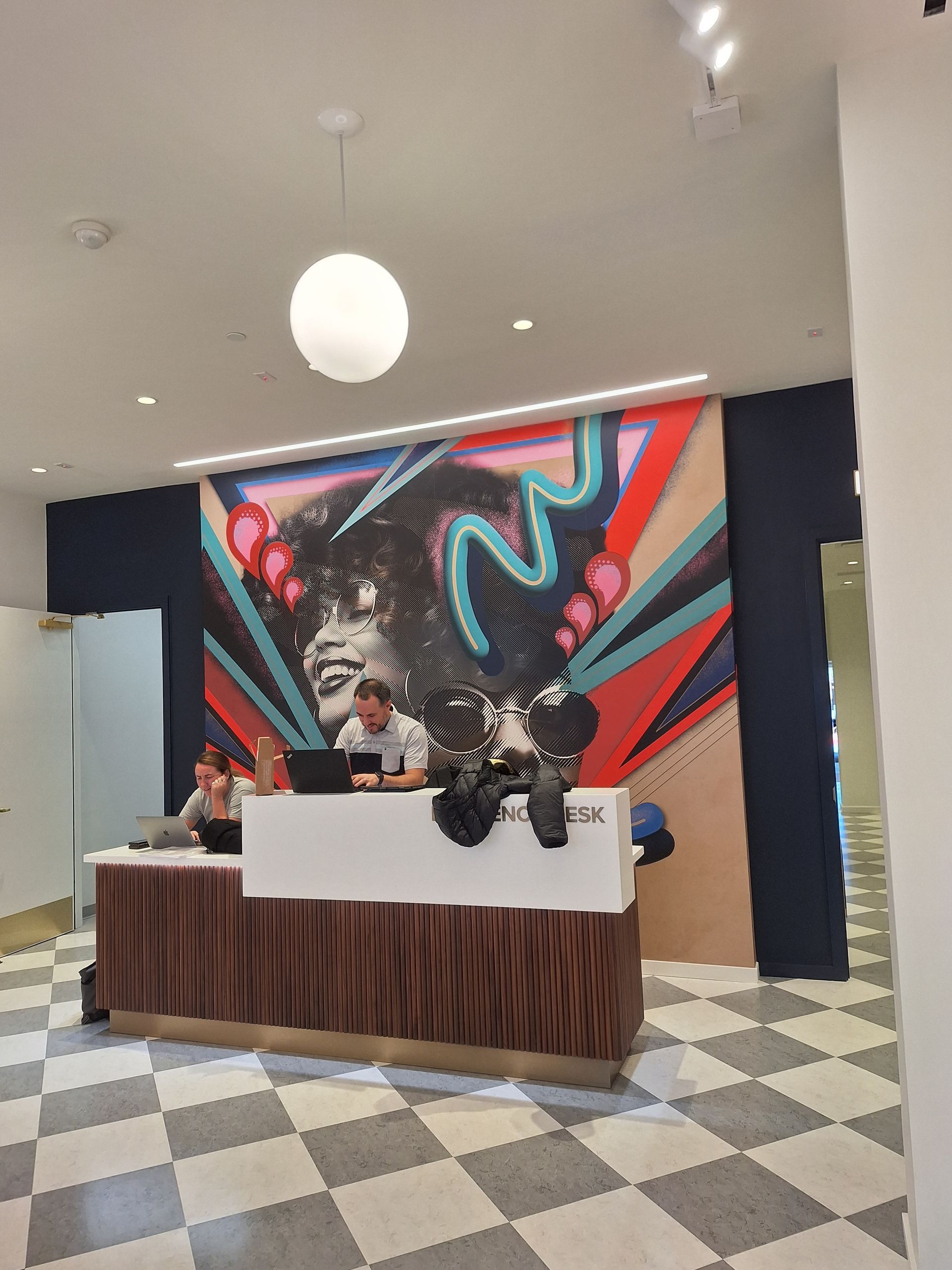 Reception desk with mural, checkered floor, staff working, and overhead lighting.