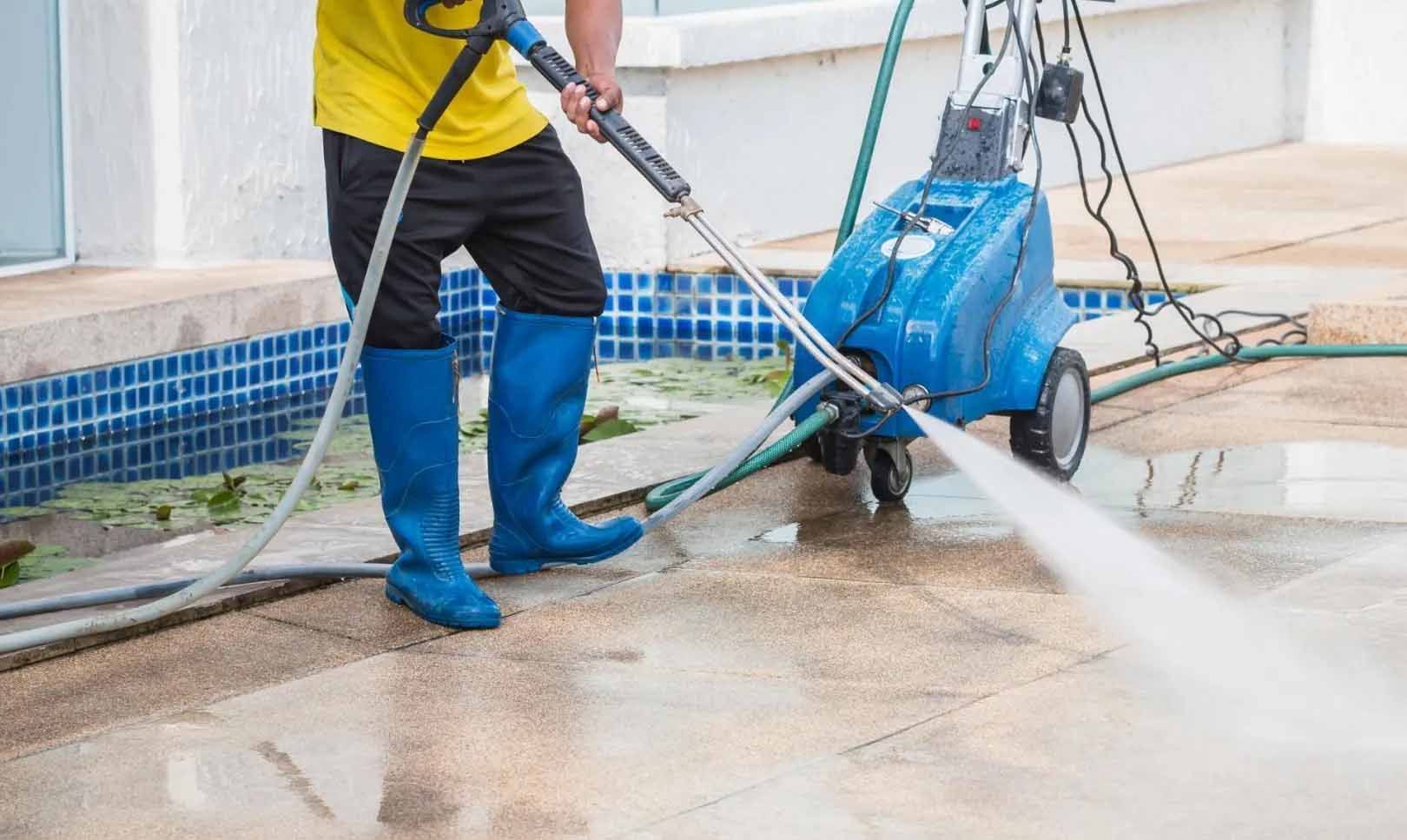 Un homme utilise un nettoyeur haute pression pour nettoyer un trottoir.