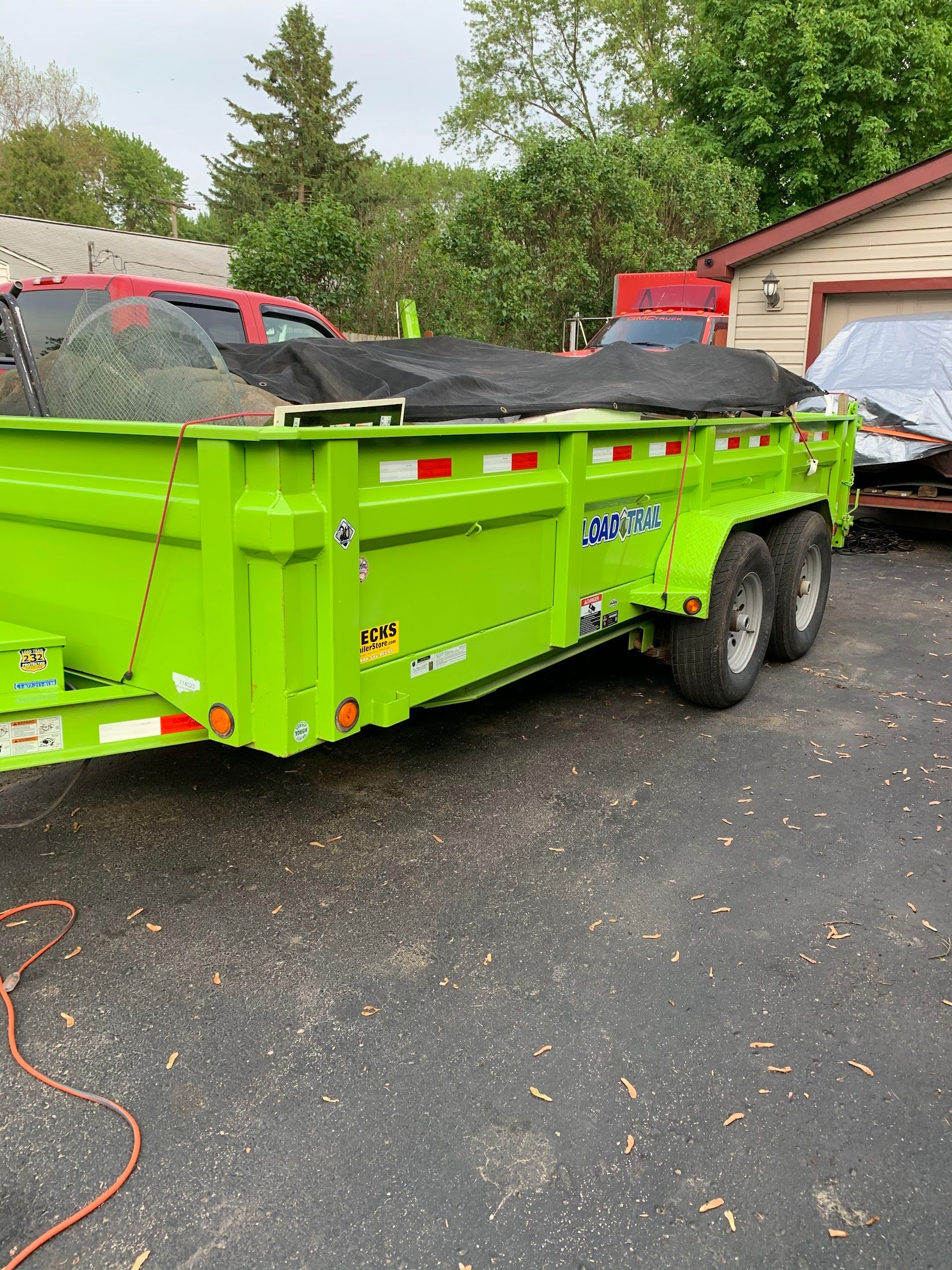 A green dump trailer is parked in a driveway next to a house.