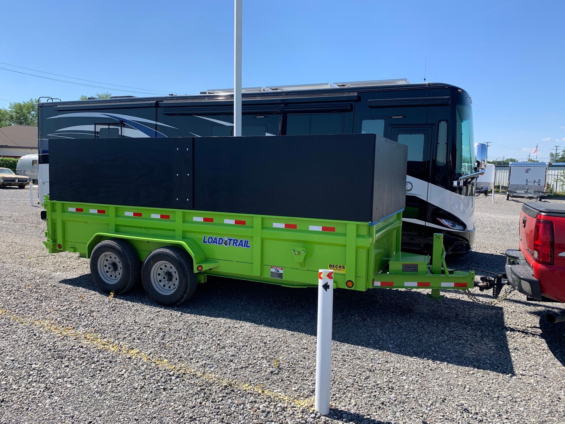 A green trailer is attached to a bus in a gravel lot.