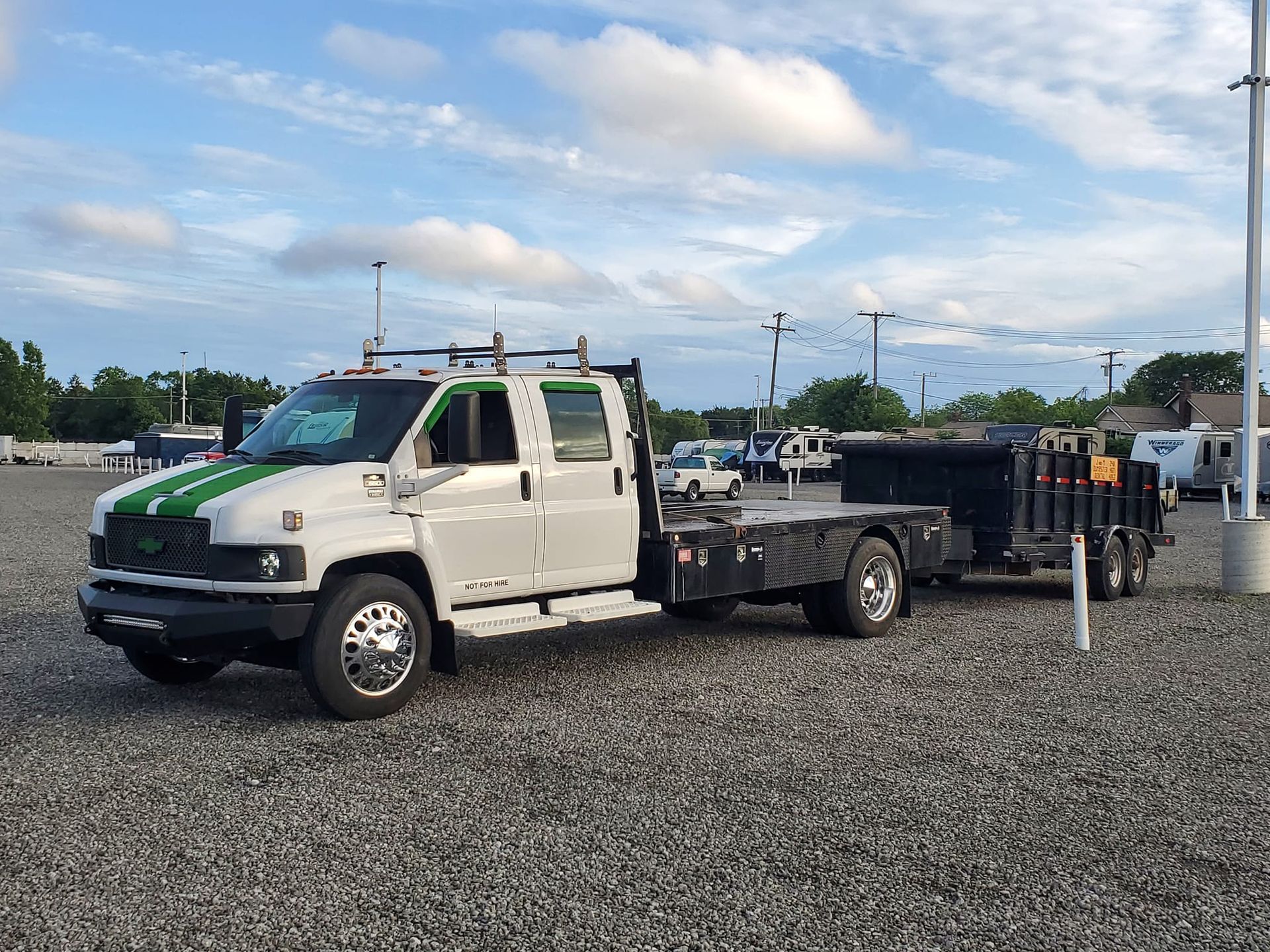 A white truck with a trailer attached to it is parked in a gravel lot.