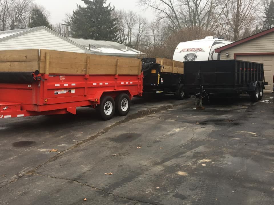 A red dump trailer is parked next to a black dump trailer in a parking lot.