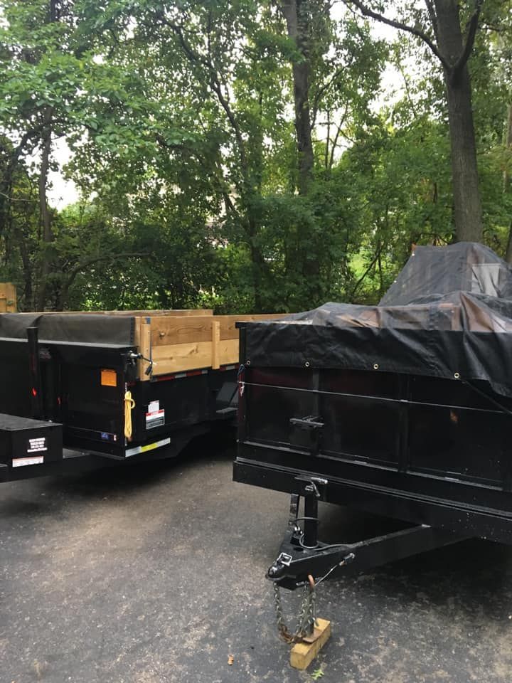 Two dump trailers are parked in a driveway with trees in the background.