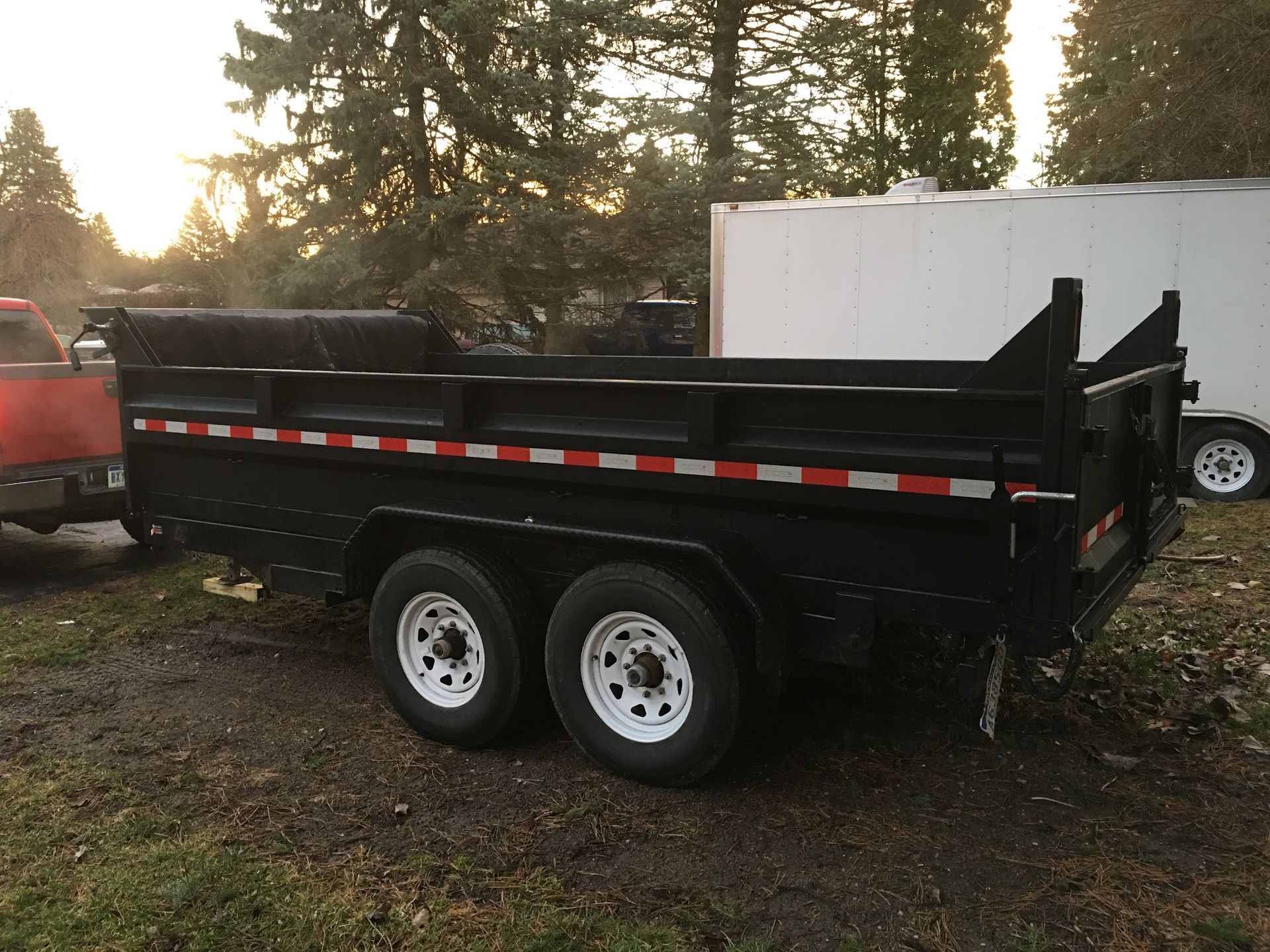 A dump trailer is parked next to a red truck.