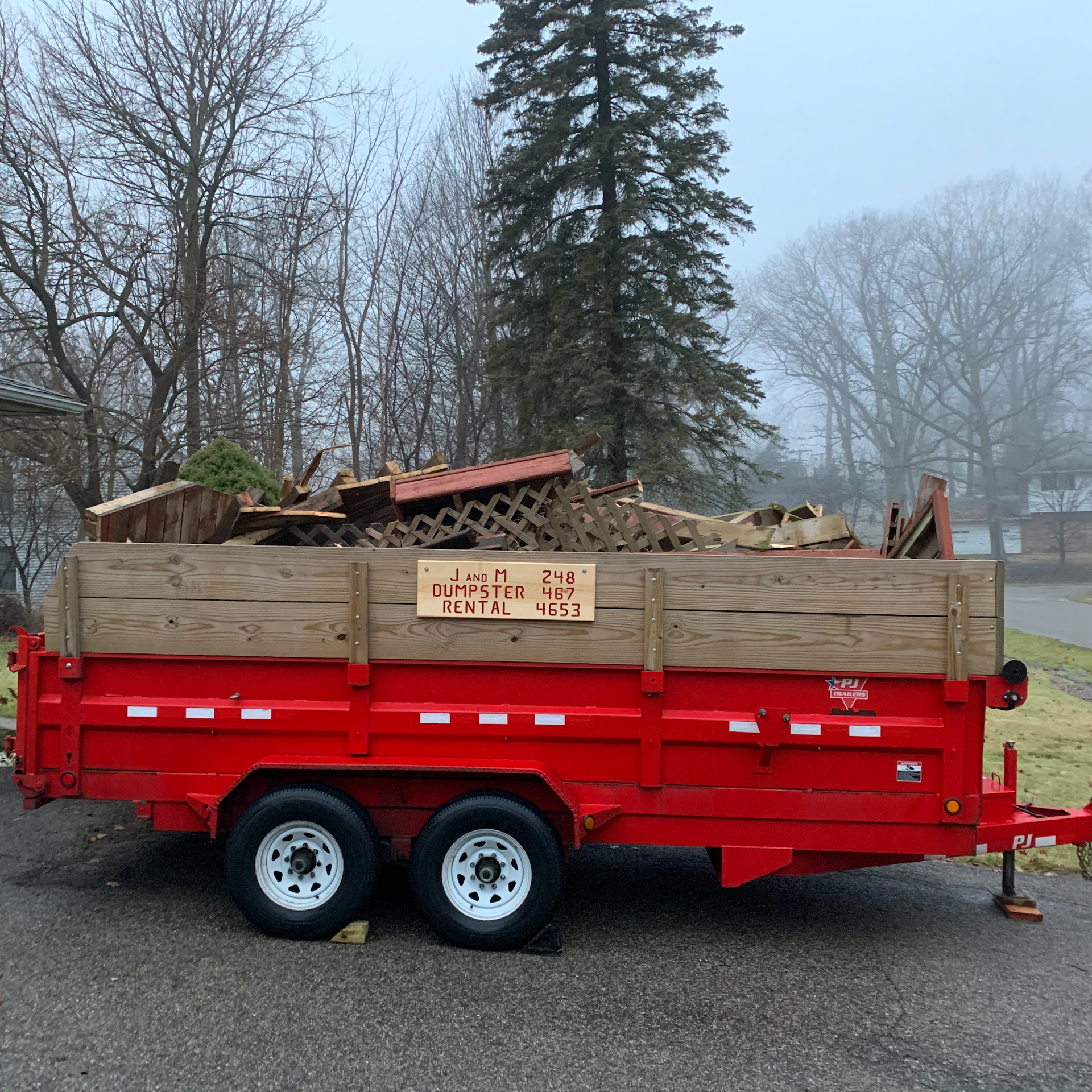 Bright green dump trailer loaded with debris, parked near a red truck and garage.