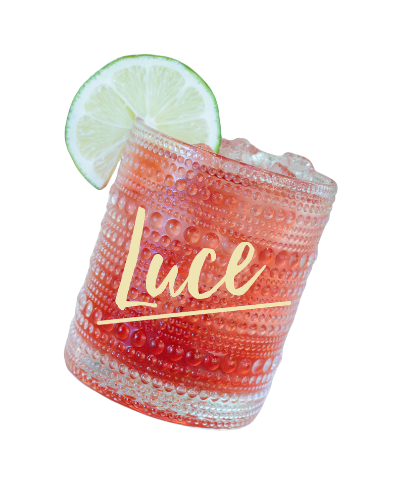 Lime-garnished red cocktail in a textured glass labeled “Luce”