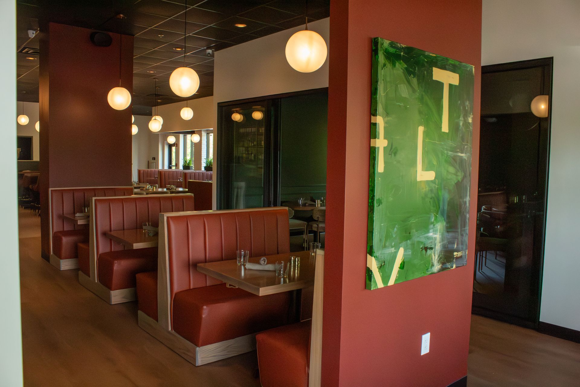 Empty restaurant booths with red seats and hanging globe lights along a narrow aisle.