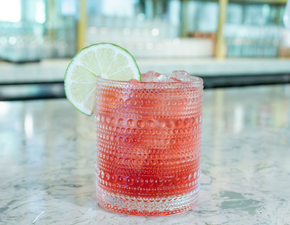 Yellow cocktail in a martini glass with pickled onions on a marble table.