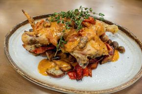 Roasted chicken atop a rustic plate of vegetables, garnished with herbs