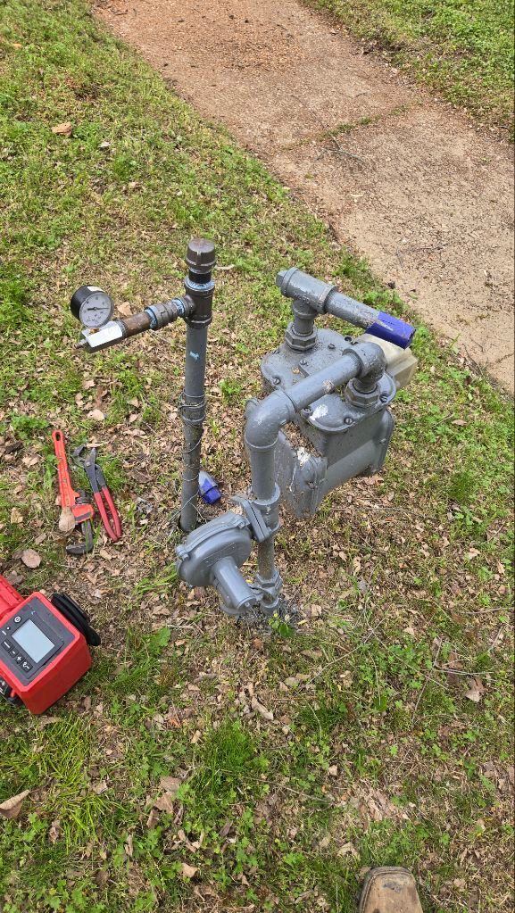 Brass irrigation backflow preventer with green-handled valves installed in the ground.