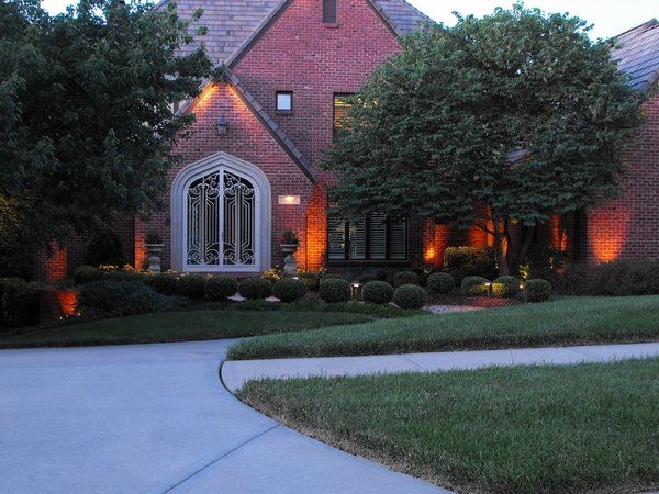 A brick house is lit up at night with trees and bushes in front of it