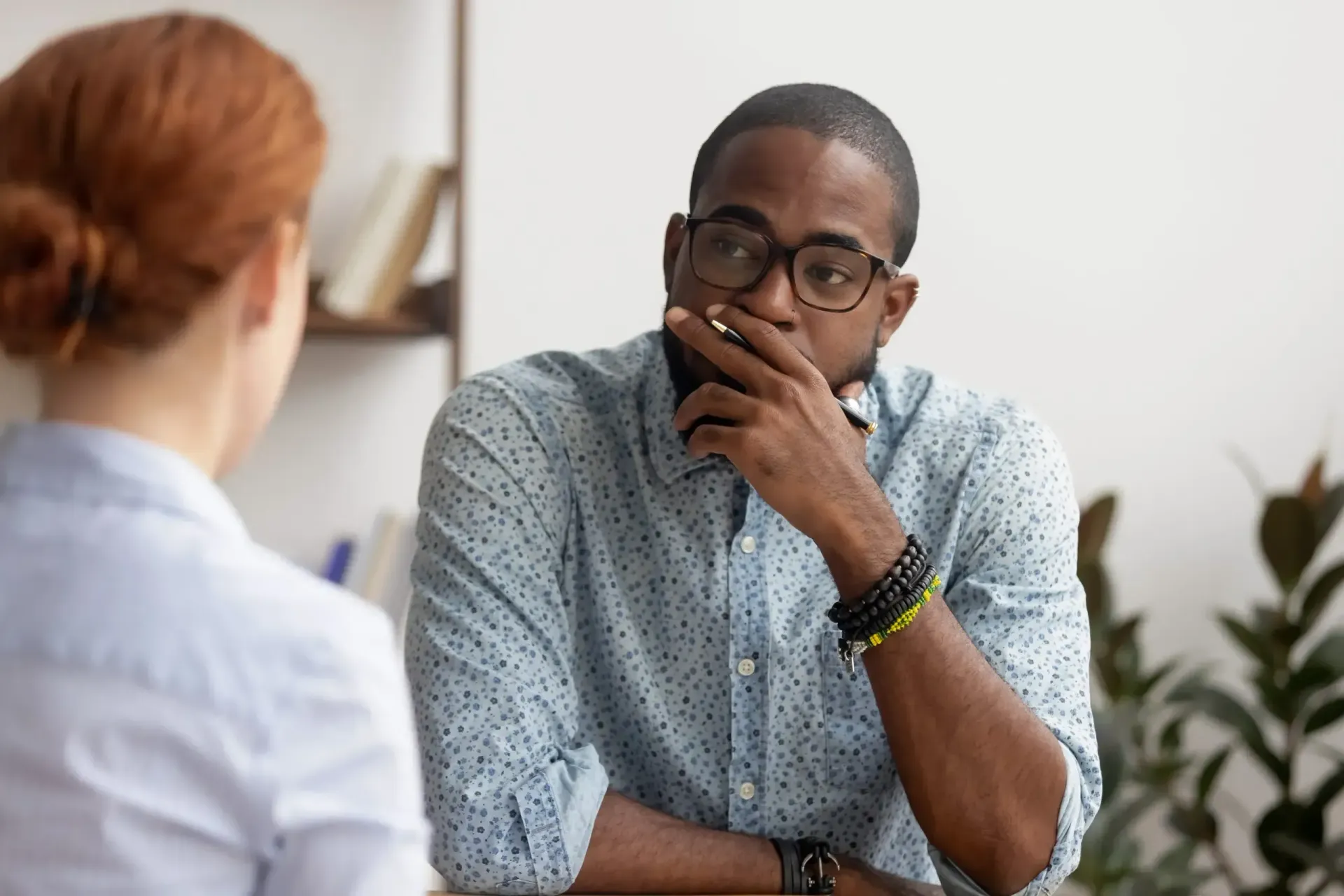 Man with glasses thoughtfully listens to a woman, indoor setting.