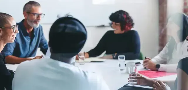People seated around a white table in a meeting, smiling and talking.