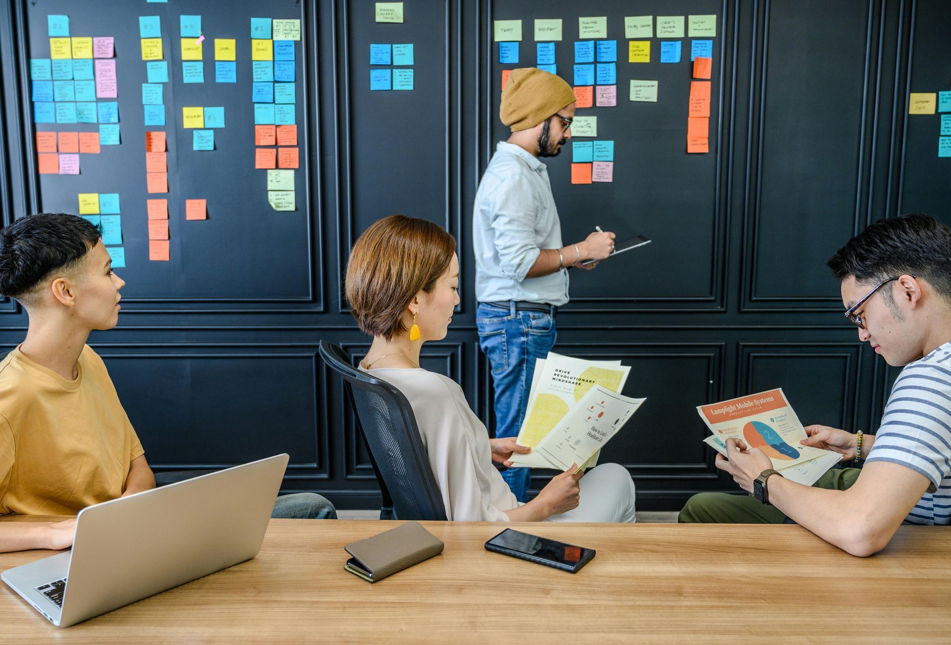 Agile Delivery Team meeting with sticky notes on a black wall, looking at charts and a laptop.