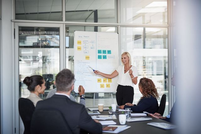 Woman presenting ideas at a whiteboard in a meeting with colleagues.