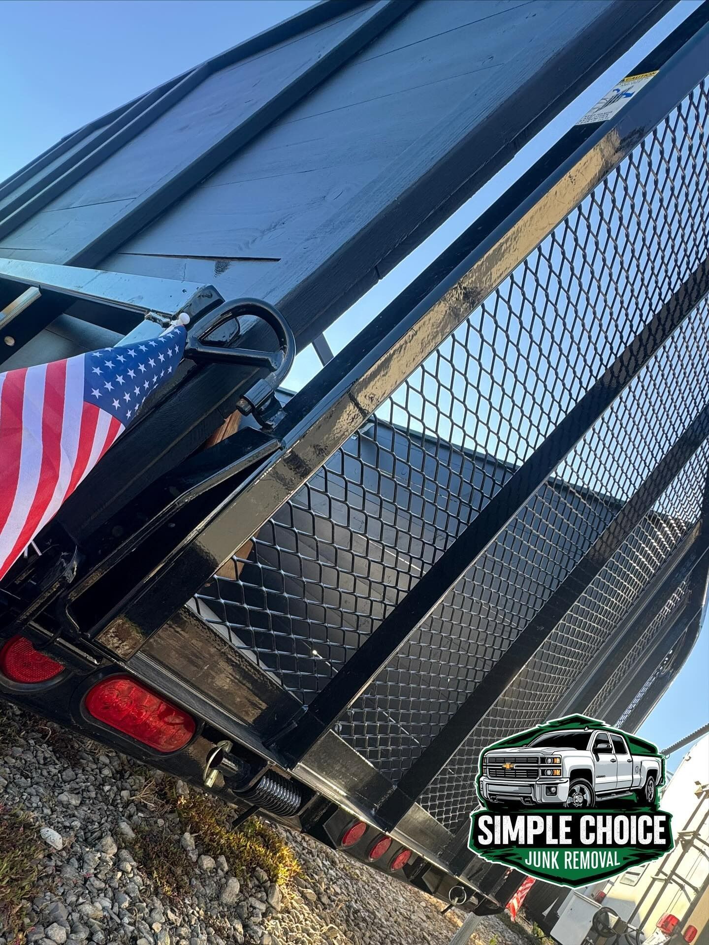 Black trailer with diamond plate floor, mesh sides, and American flag.